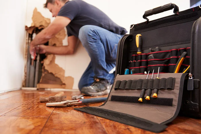 Werkzeugkiste im Vordergrund, Person repariert Wand im Hintergrund